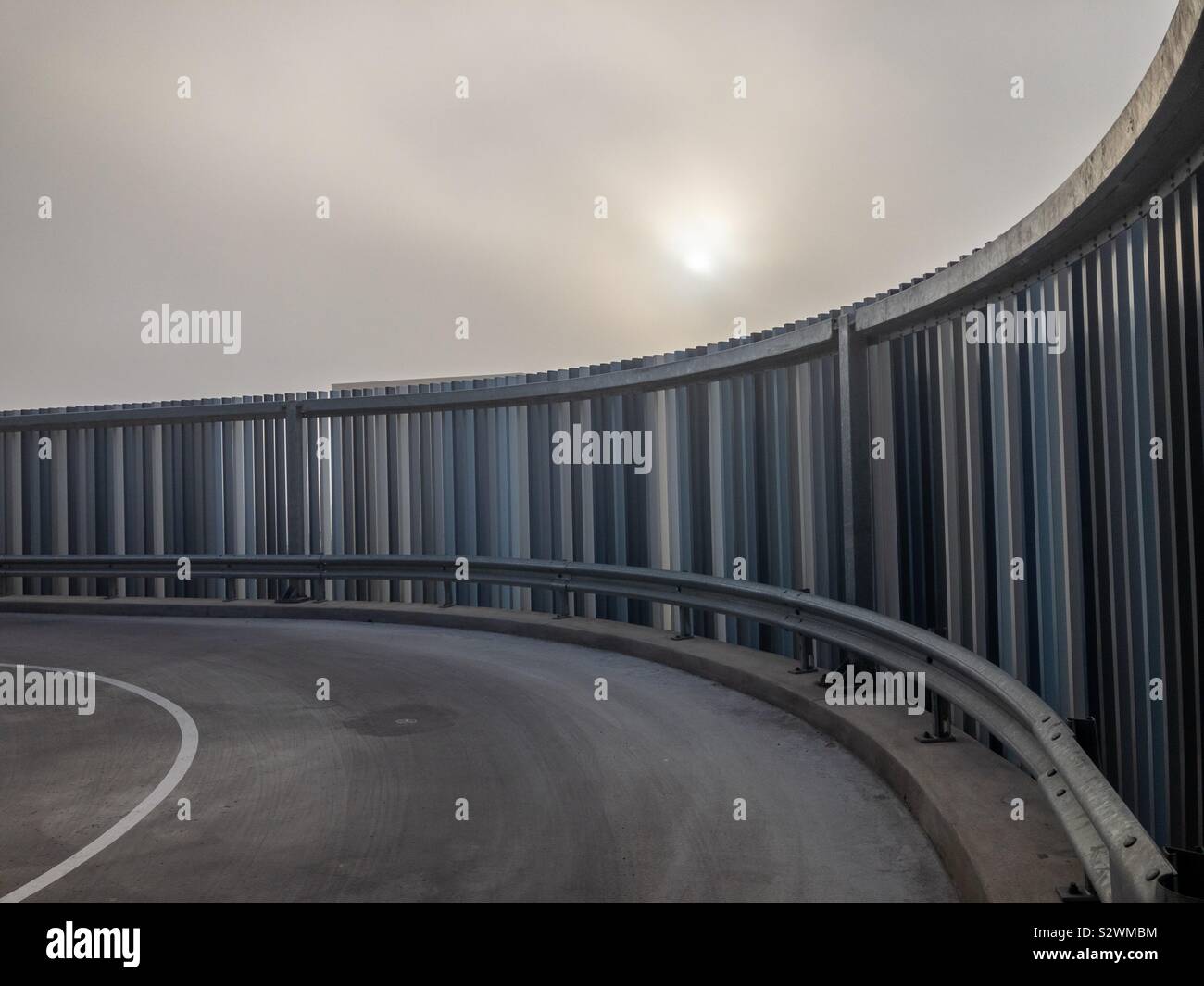 Straße und Metall Zaun im Morgennebel. - Smartphone-aufgenommenes Stockfoto