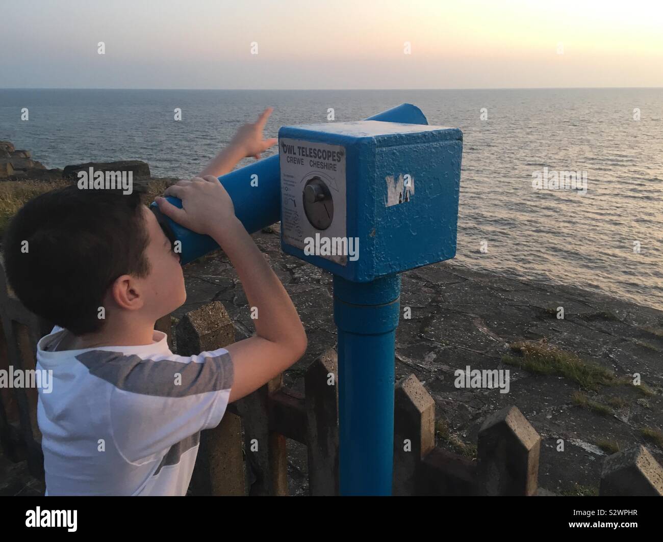 Ein 9-jähriges Kind mit Meerblick durch ein Teleskop auf der Promenade in Blackpool. Stockfoto