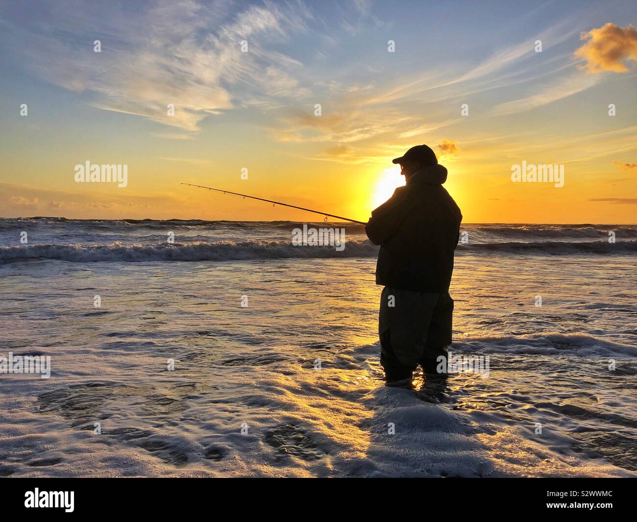 Silhouetted angler Fischen bei Sonnenuntergang auf llangennith Strand, Gower, Swansea, South West Wales, August. Stockfoto