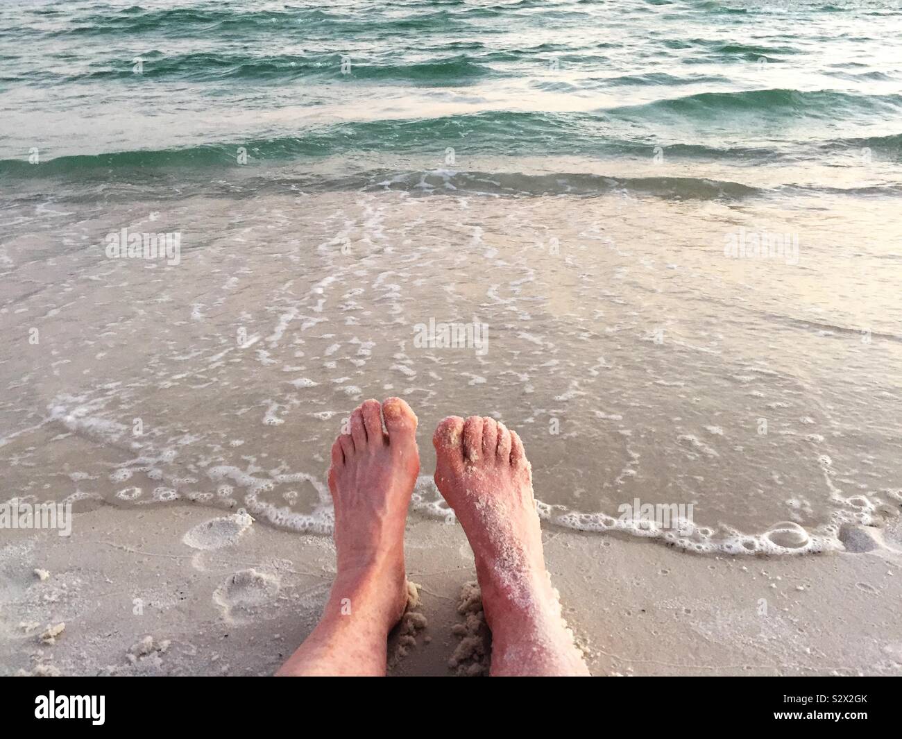 Ein Weibchen ist gemütlich sitzen im Sand am Wasser. Ihre Füße sind mit dem weißen Sand vom Strand an den Golf von Mexiko. Stockfoto