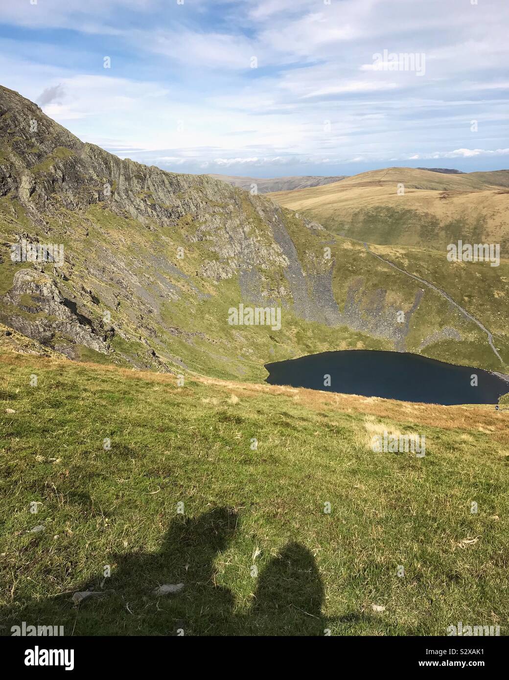 Schatten von zwei Menschen, die auf ihrer Wanderung auf einen Berg mit Blick auf einen kleinen Tarn - Smartphone-aufgenommenes Stockfoto