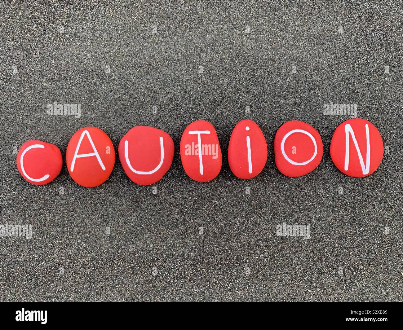 Vorsicht Text mit rot gefärbten Steine über schwarzen vulkanischen Sand - Smartphone-aufgenommenes Stockfoto