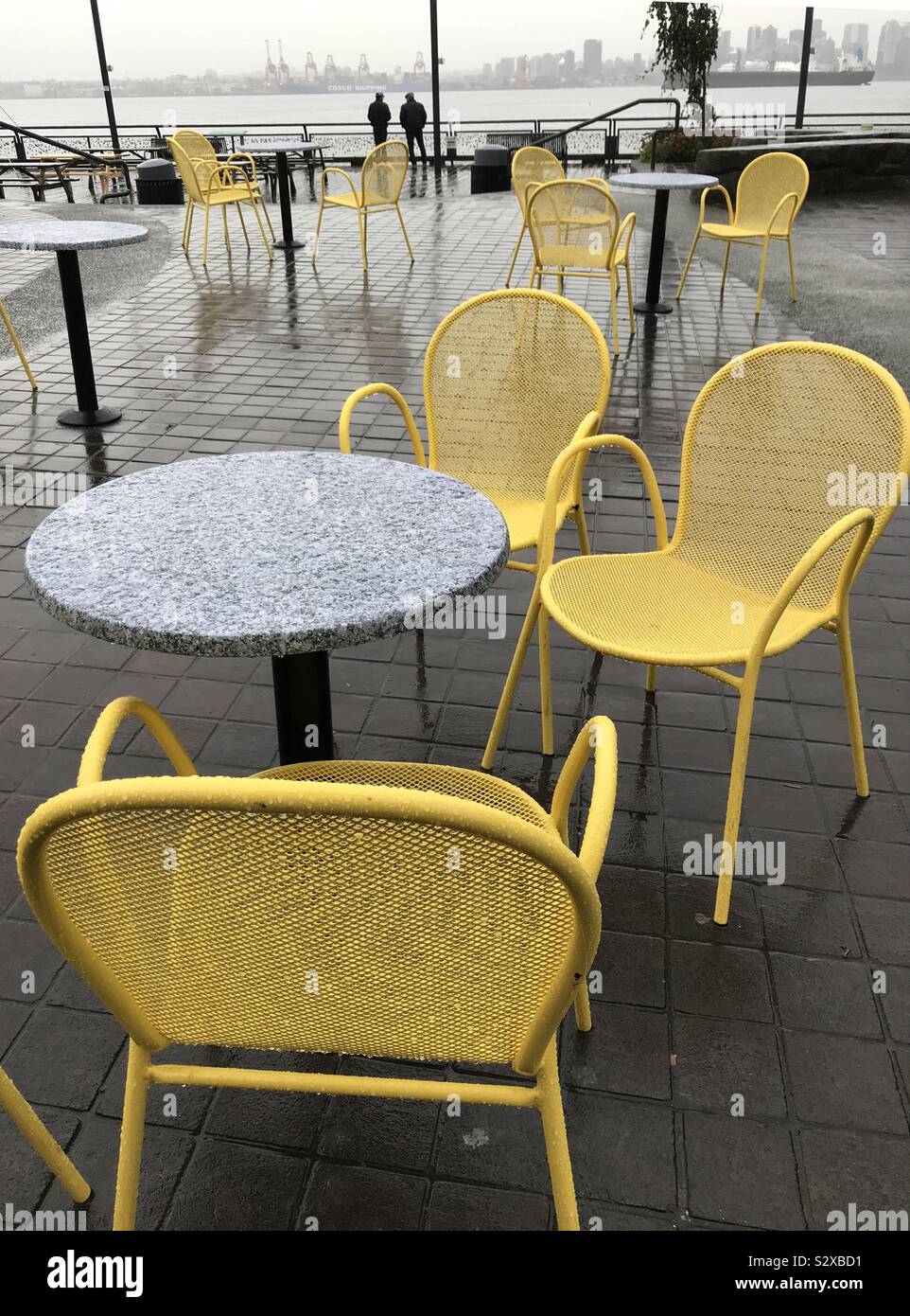 Bunte leere Stühle und Tische auf einem grauen regnerischen Tag in North Vancouver mit Blick auf das Wasser. Stockfoto