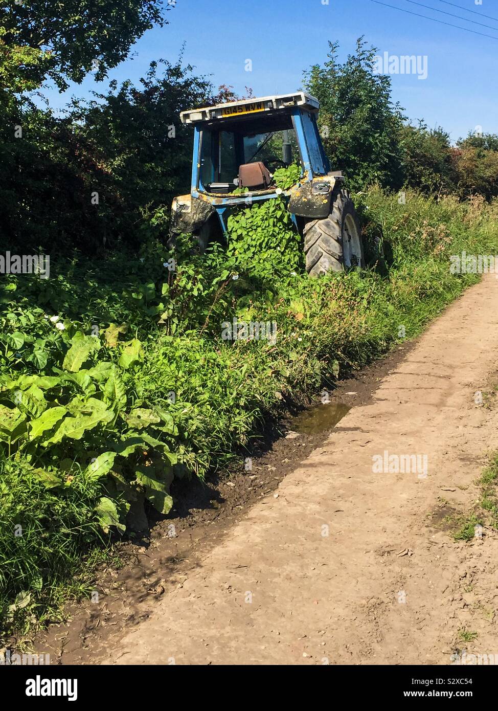 Ein Traktor liegt auf der Straße verlassen, und mit Unkraut überwuchert. Stockfoto