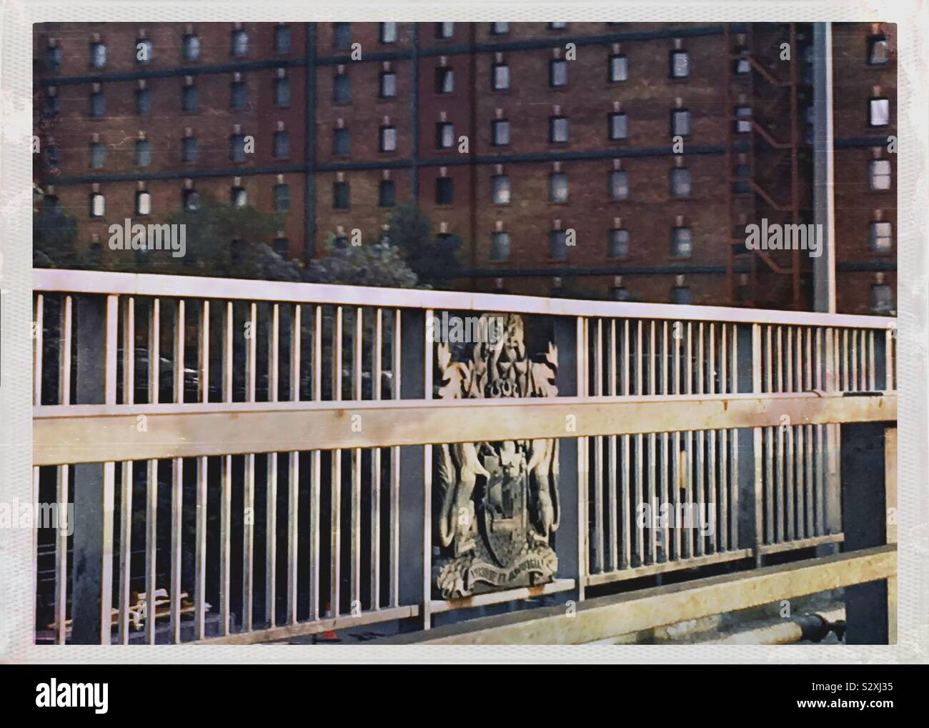 Ein Wappen auf Metall Geländer auf dem Plimsoll Brücke in Bristol, mit einem alten verklebt Tobacco Warehouse im Hintergrund Stockfoto