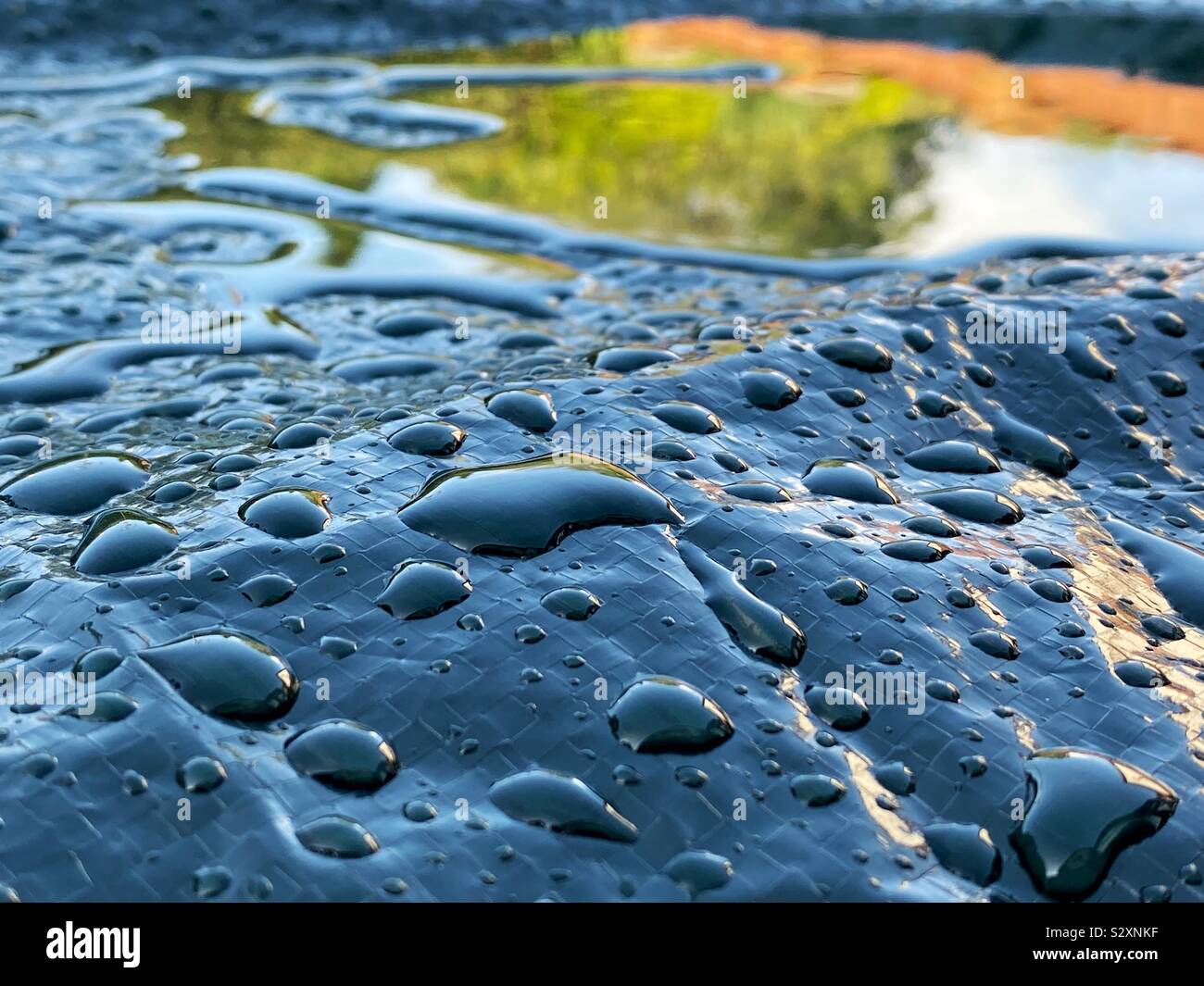 Regentropfen und Wasser stehend auf einer Kunststoffabdeckung für Gartenmöbel Stockfoto