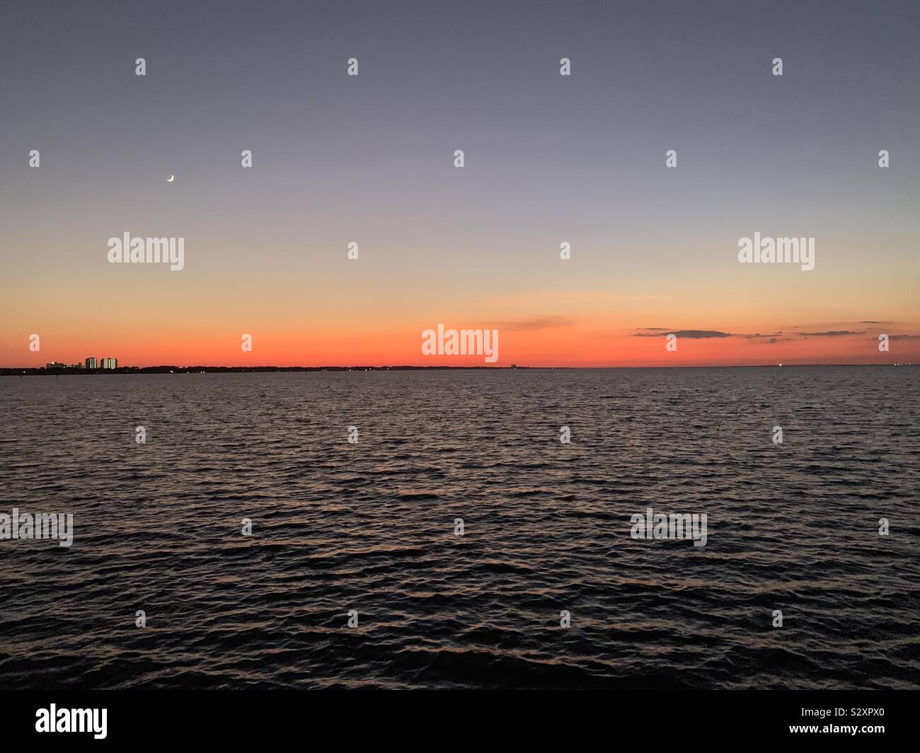 Bis spät in die Nacht Sonnenuntergang über der Bucht Wasser mit bunten Himmel und entfernten Stadt scape - Smartphone-aufgenommenes Stockfoto