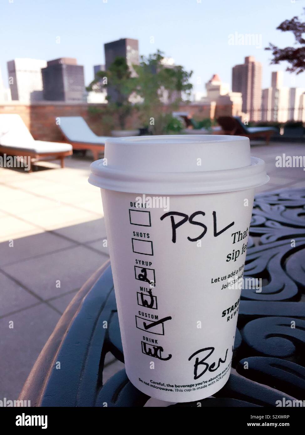Nehmen Sie Tasse Starbucks pumpkin Spice latte auf einem Tisch in einem städtischen Dachterrasse Garten, NYC, USA - Smartphone-aufgenommenes Stockfoto