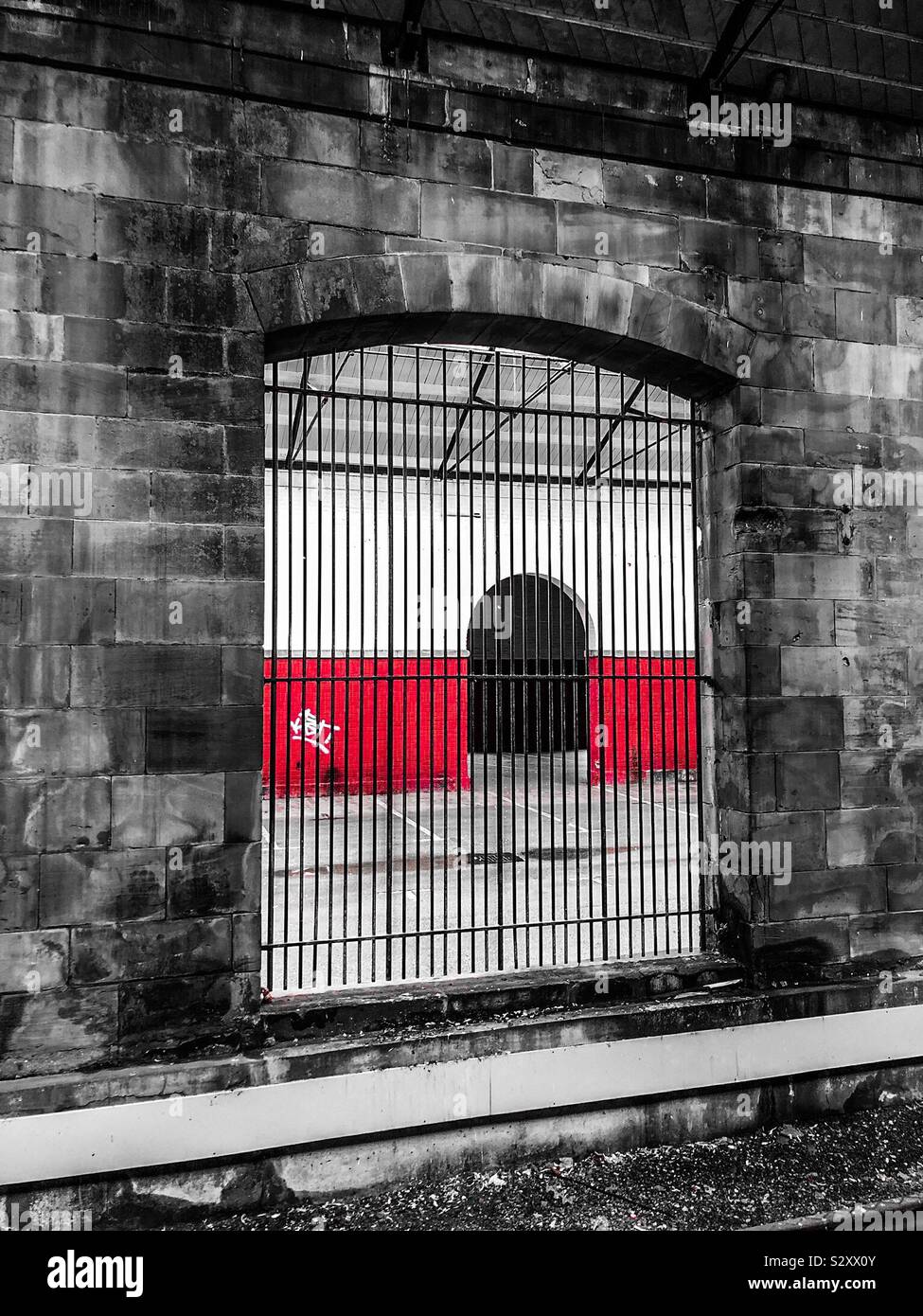 Metallgitter in einem alten Rauch-bedeckten Mauer aus Stein mit Blick auf die rot lackierten Wand- und Graffiti Stockfoto
