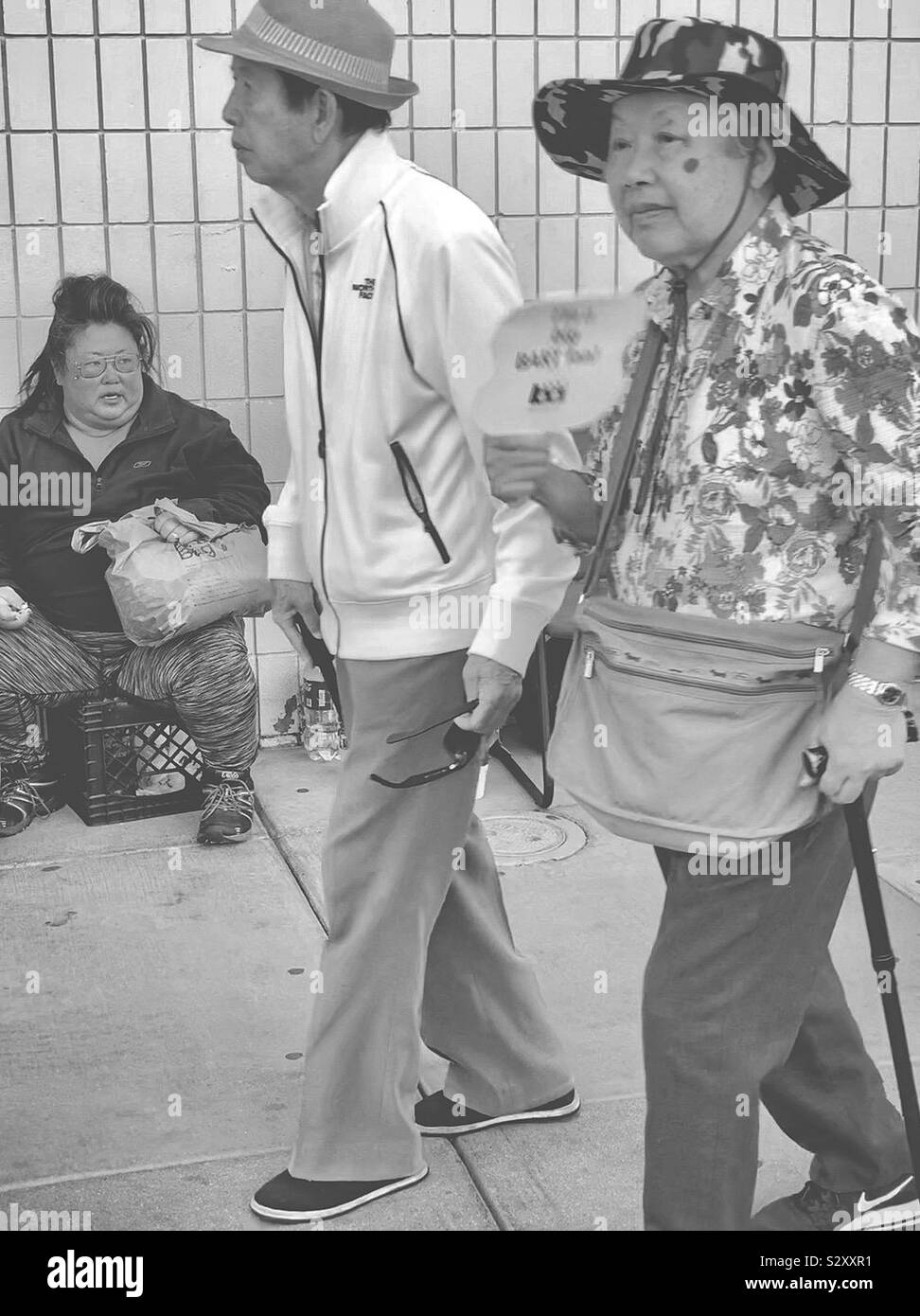 Eine asiatische Fett obdachlose Frau sitzt auf einer Straße herum zu schauen, während die alten asiatischen Paar vorbei sind. Stockfoto