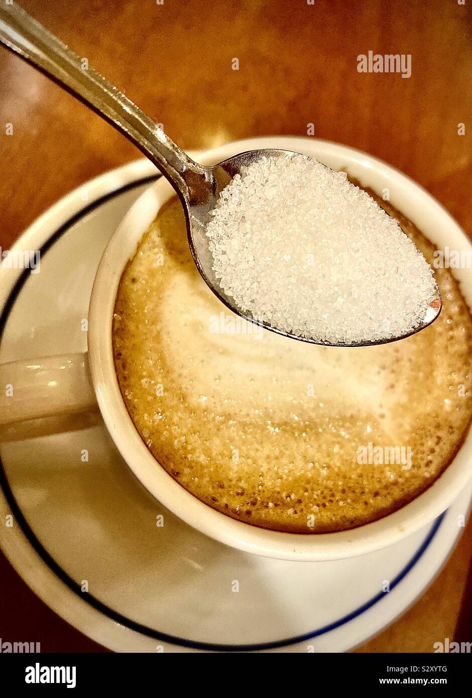 Teelöffel mit Zucker halten bei einer Tasse Cappuccino Stockfoto