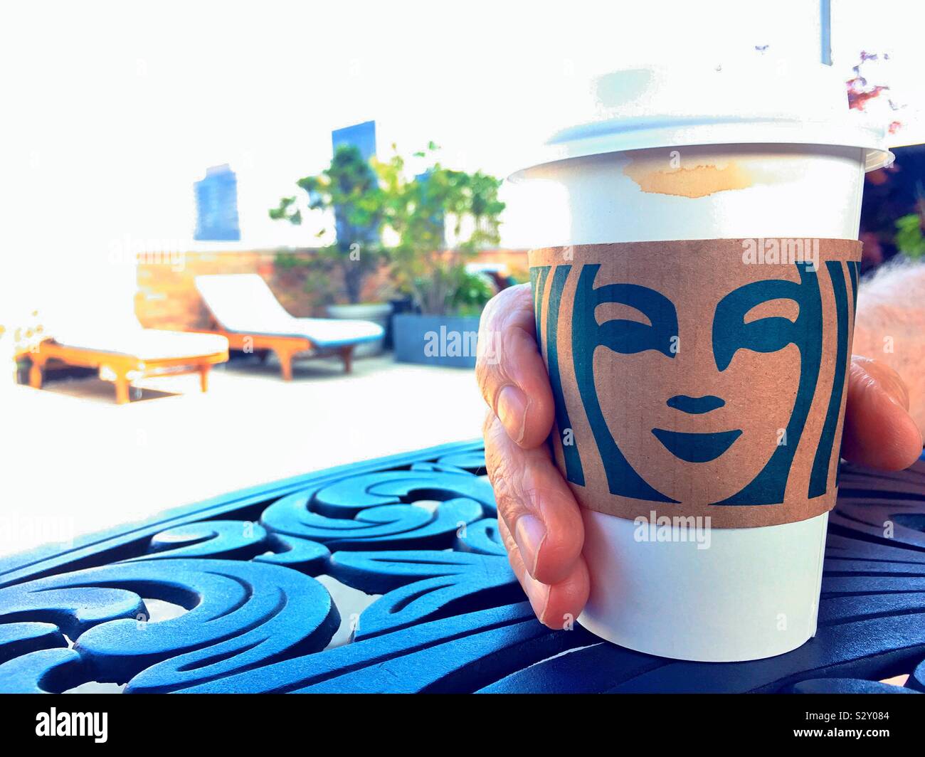 Mann genießen eine Tasse Kaffee von Starbucks mit einer Hülse aus Pappe auf seiner Dachterrasse Terrasse in Midtown Manhattan, New York City, USA Stockfoto