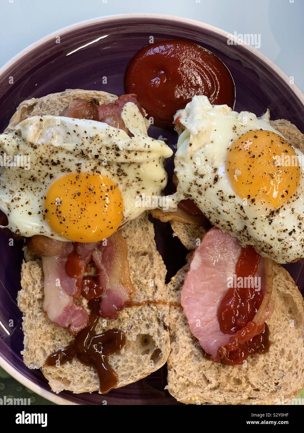 Speck, Eier und Würstchen in einer weiche braune Bun halb und halb Tomatenketchup und Braune Soße Stockfoto