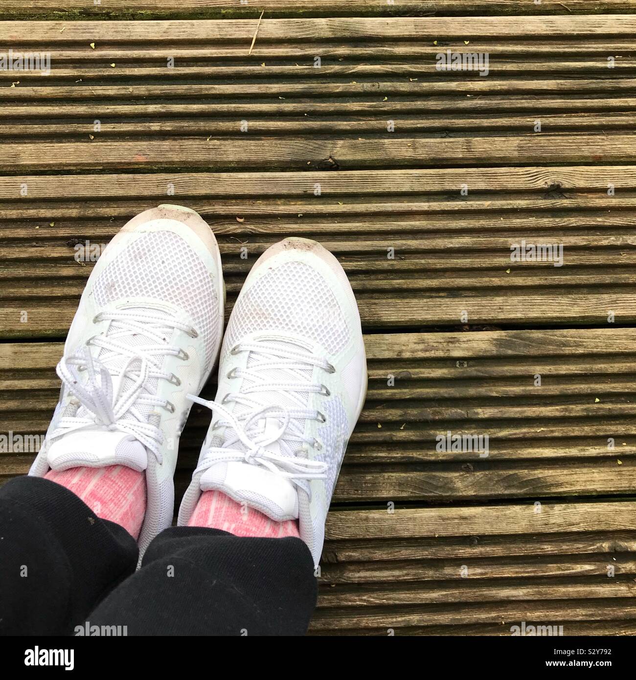 Meine Damen Füße in Weiß Trainer und Jogging Hose auf Holzterrasse Stockfoto