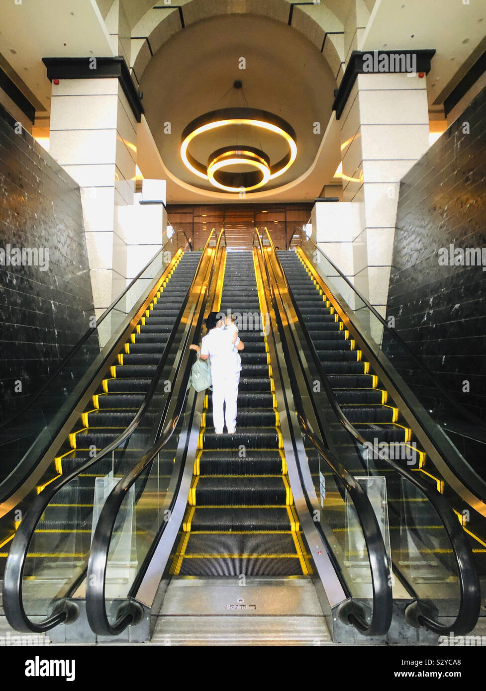 Rolltreppe in der Symmetrie mit architektonischen Innen Dame trägt Baby Stockfoto
