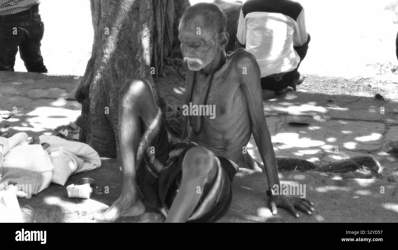 Geschlagen von Live ein alter Mann sitzt unter einem Baum neben Ganga und Es ghats. Stockfoto