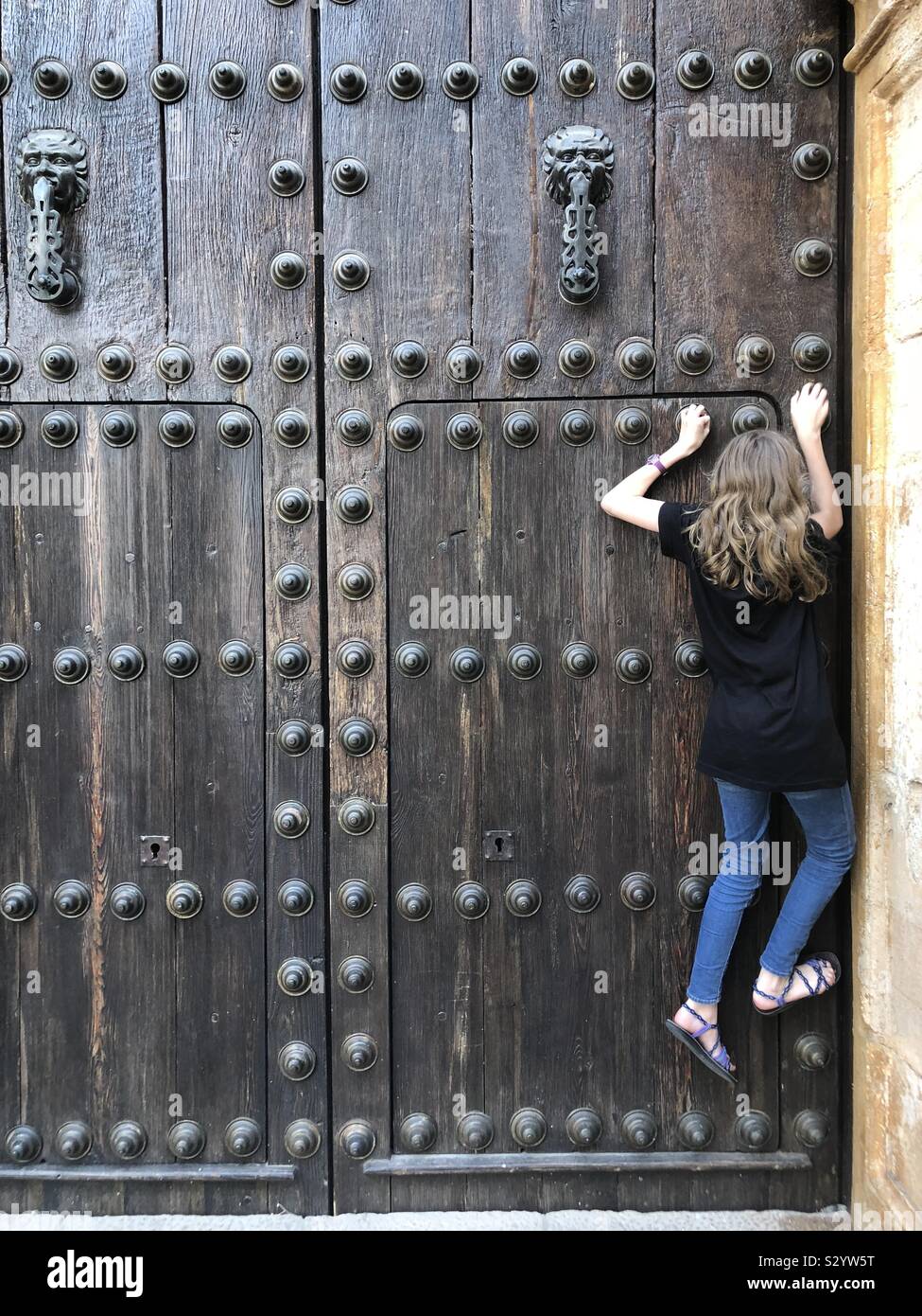 Mädchen, die versuchen, die türklopfer auf eine riesige Tür zu erreichen, Stockfoto