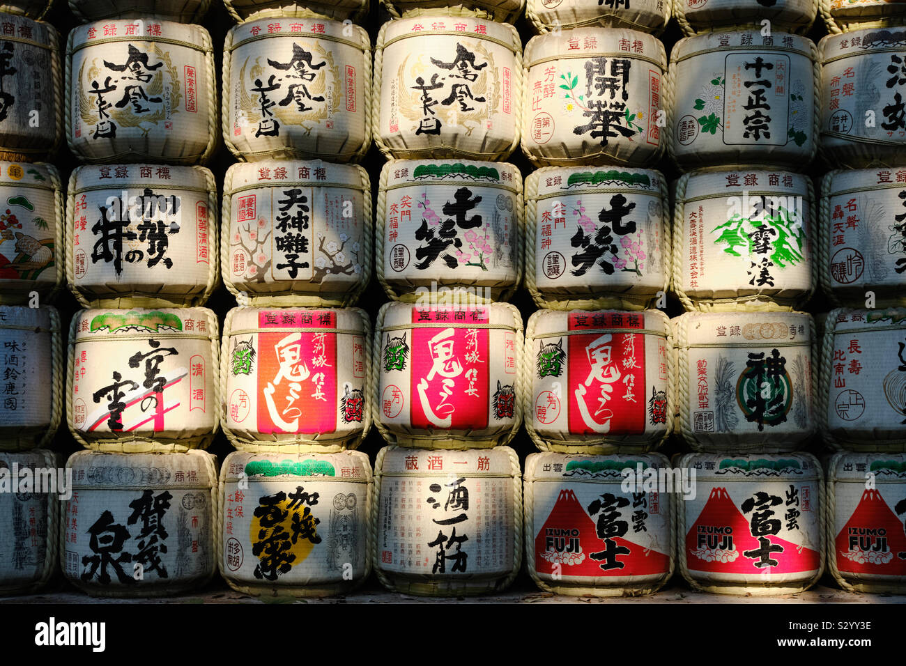 Zeilen von Sake Fässer auf einander im Freien in natürliche Beleuchtung von Tuch mit japanischen Designs und Schreiben eingerichtet gewickelt gestapelt. Stockfoto