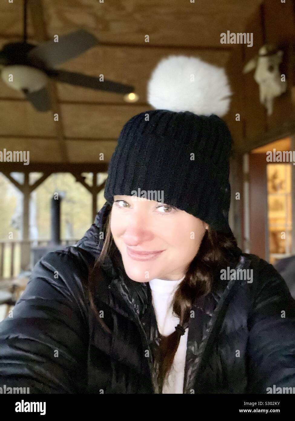 Frau mit geflochtenem Haar & Winter Fell Ball Cap lächelnd an einem Land, Kabine Stockfoto