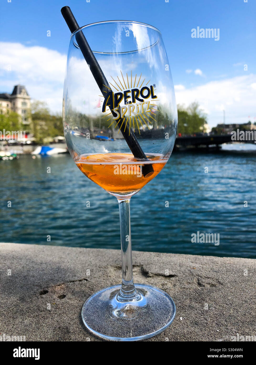 Halb leer Aperol Spritz Glas mit Stroh und Blick auf den Zürichsee Stockfoto