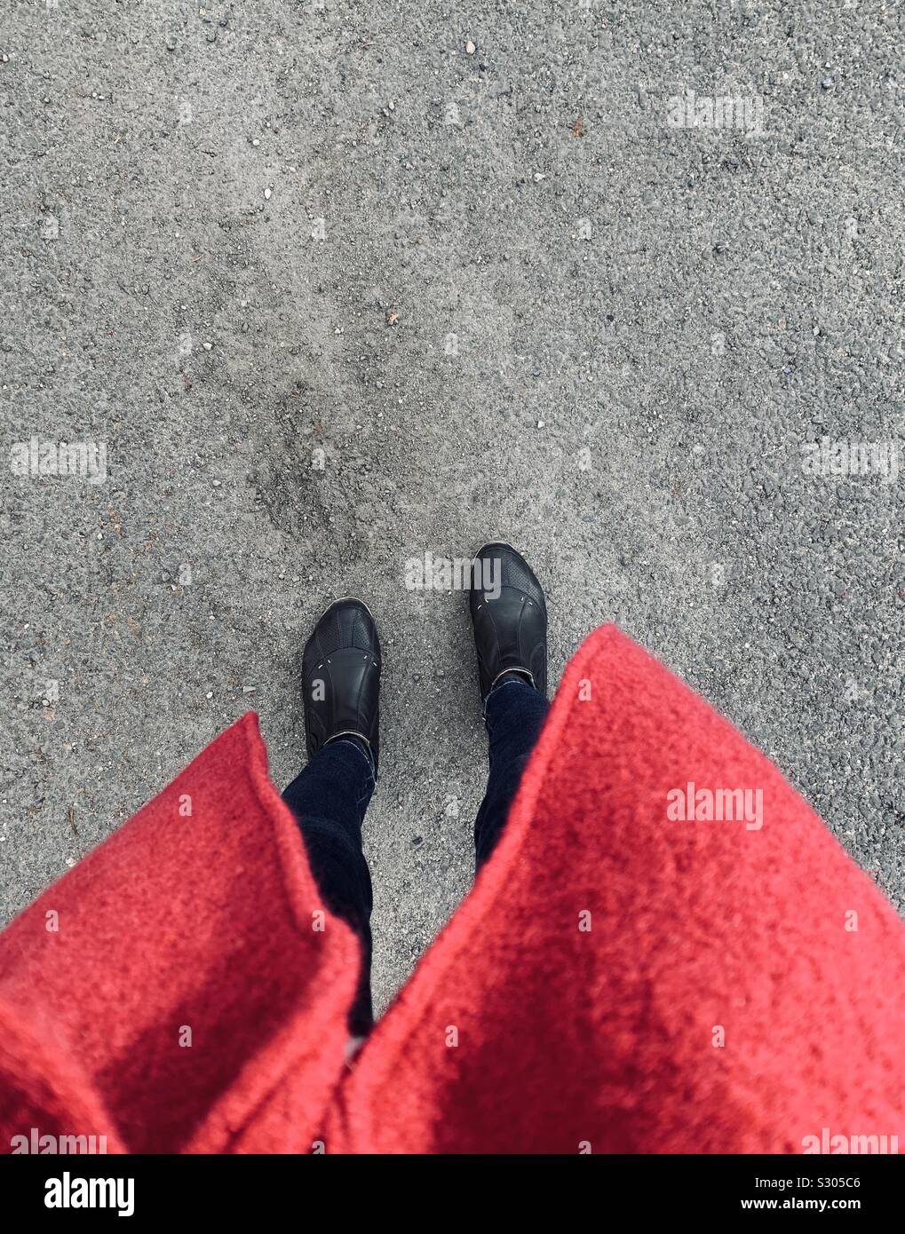 Dreckige Asphalt im Gegensatz zu schwarzen Schuhen und roten Mantel Stockfoto