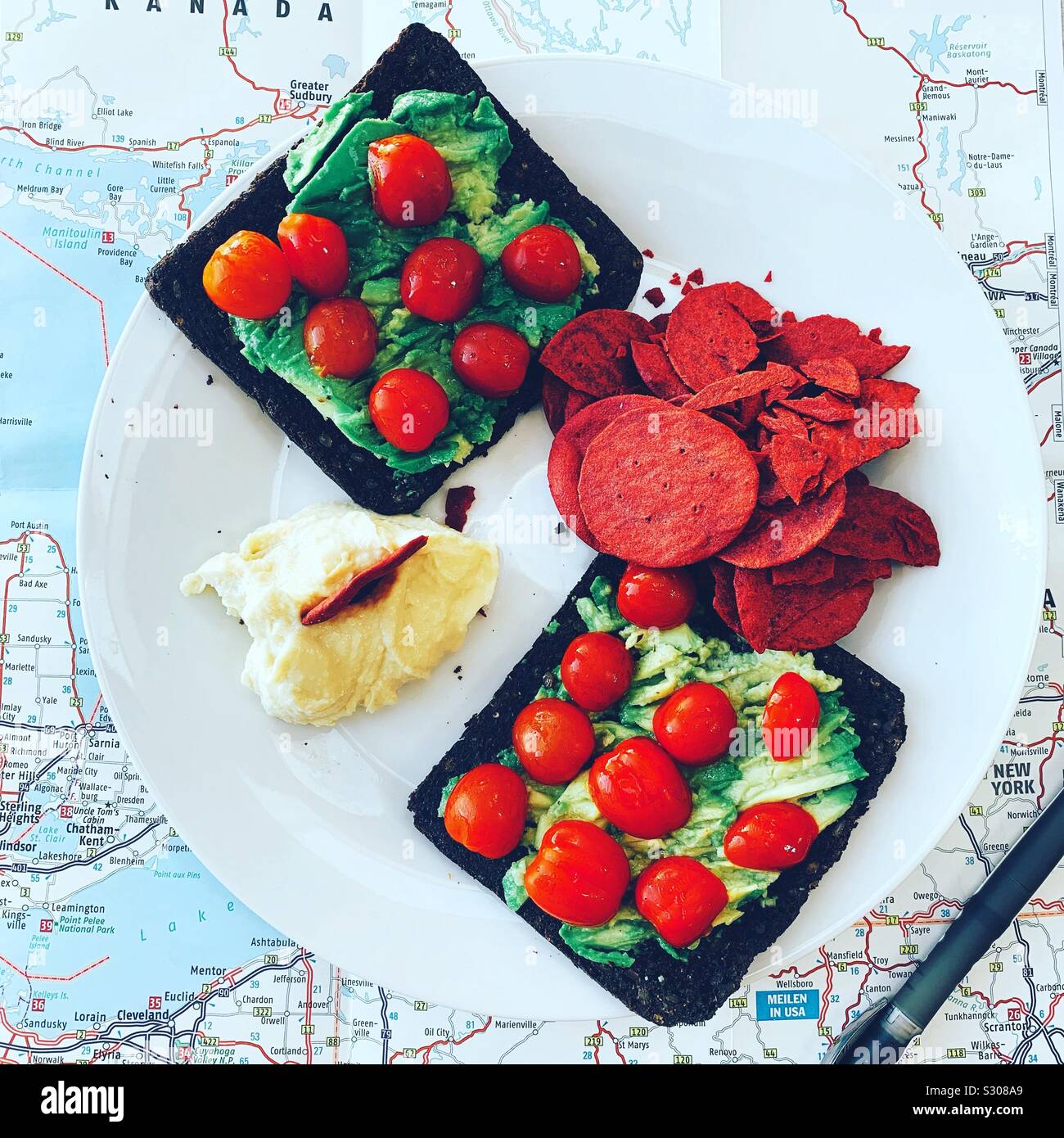 Frühstück: Pumpernickel, Avocado, Tomaten, Chips, Hummus. Stockfoto