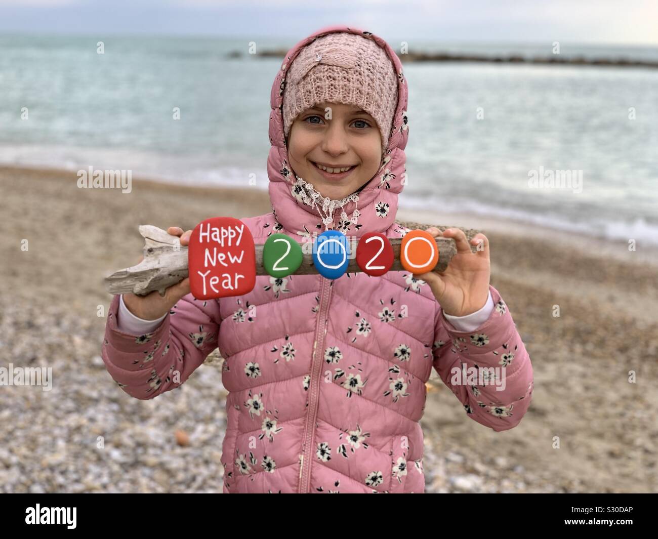 Frohes Neues Jahr 2020 mit einem Kind mit einem kreativen bunten Steine Zusammensetzung am Strand Stockfoto