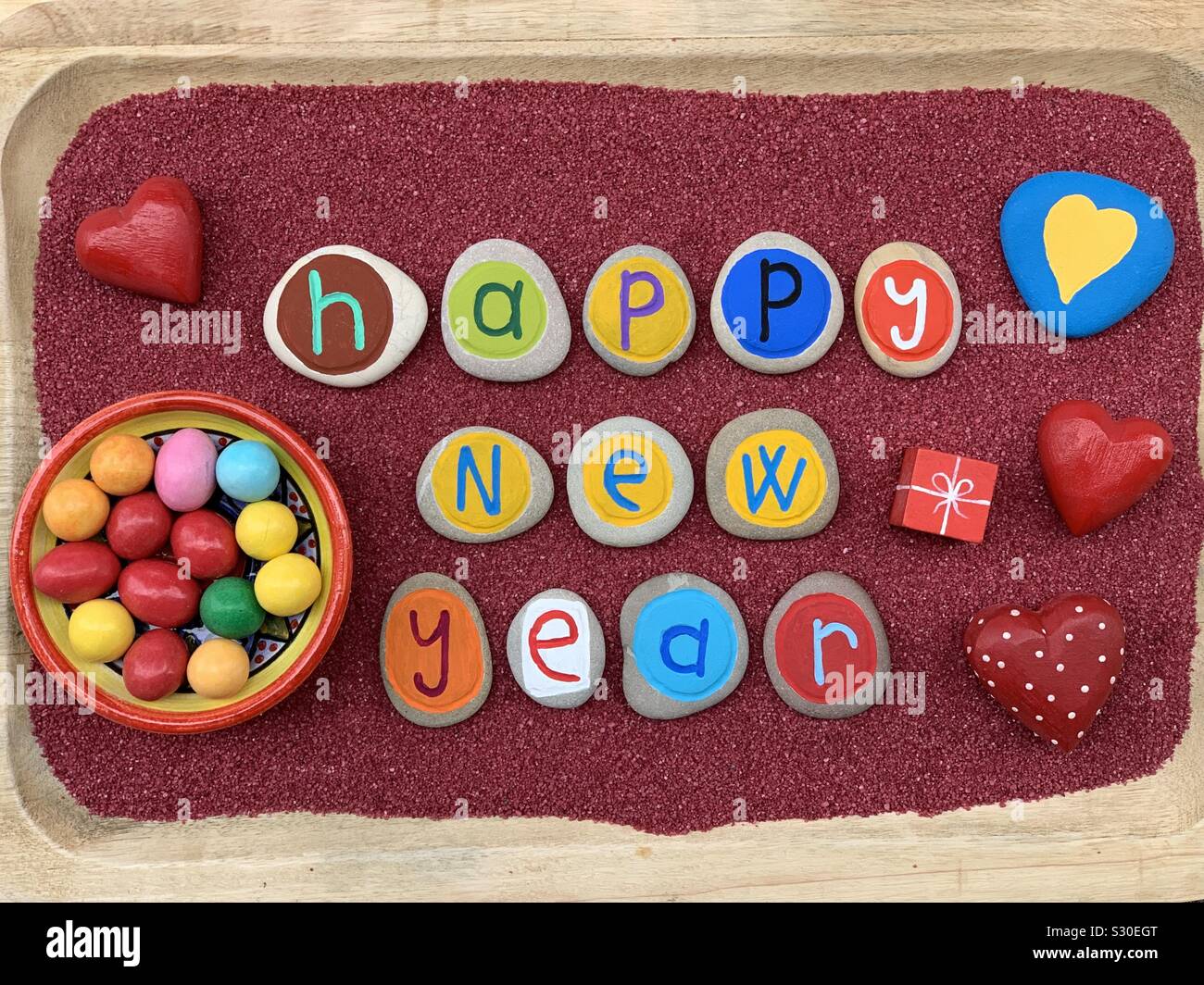 Frohes Neues Jahr wmessage mit kreative Stein gefärbt und geschnitzten Buchstaben über roten Sand Stockfoto