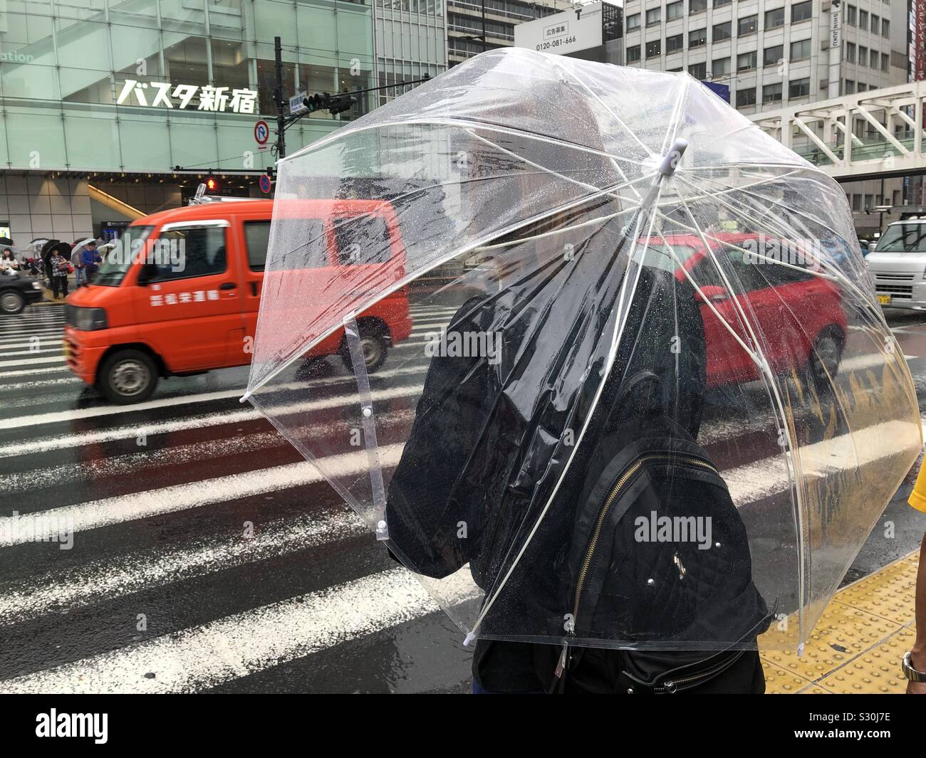 Frau unter einem Siehe durch Plastik Regenschirm warten an einem Zebrastreifen in Tokio, Japan. Stockfoto