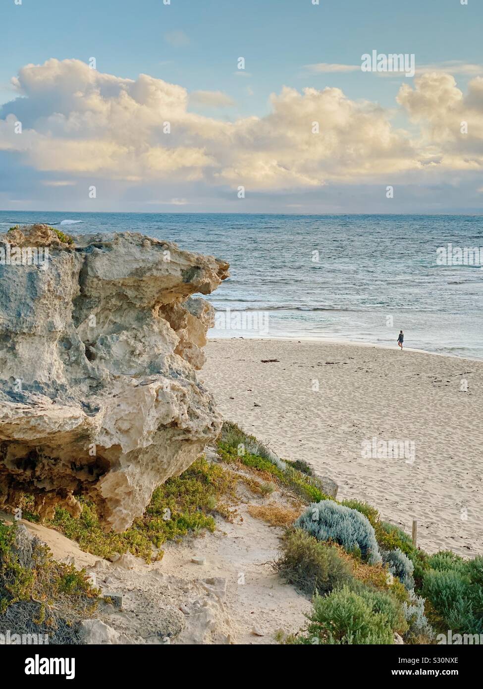Einsame Frau wandern bei Sonnenuntergang am Strand von Surfers Point, Prevelly, Western Australia. November 2019. Felsvorsprung im Vordergrund. Stockfoto