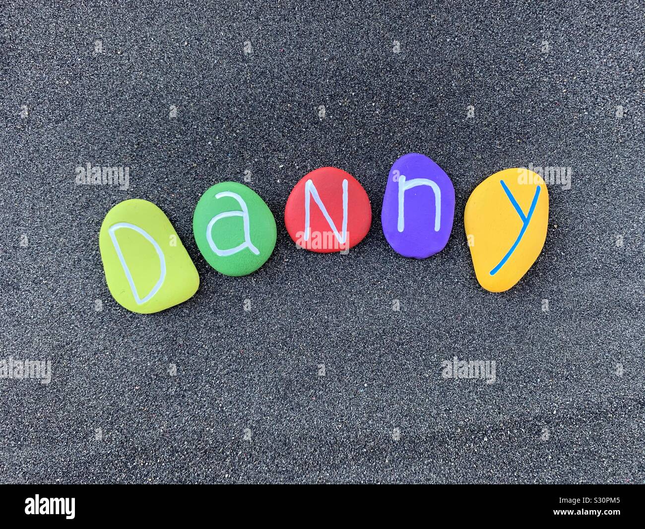 Danny, kurz für die männliche Name Daniel, komponiert mit bunten stein Briefe über schwarzen vulkanischen Sand Stockfoto