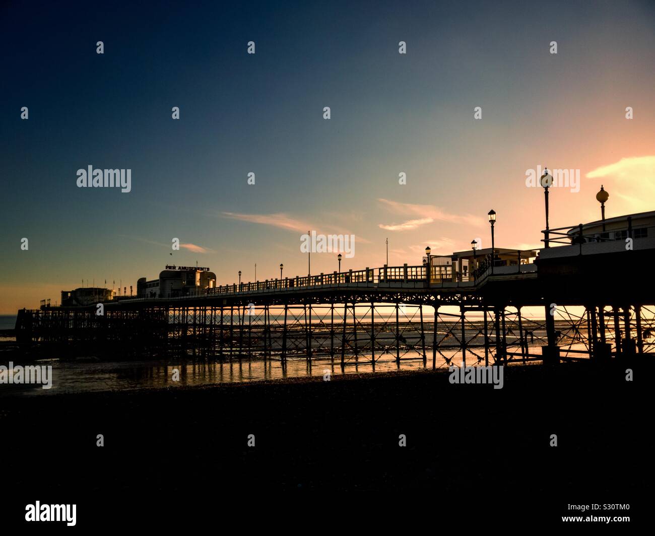 Bei Ebbe geht die Sonne hinter dem Pier in Worthing, West Sussex, England, Großbritannien, unter. - Smartphone-aufgenommenes Stockfoto