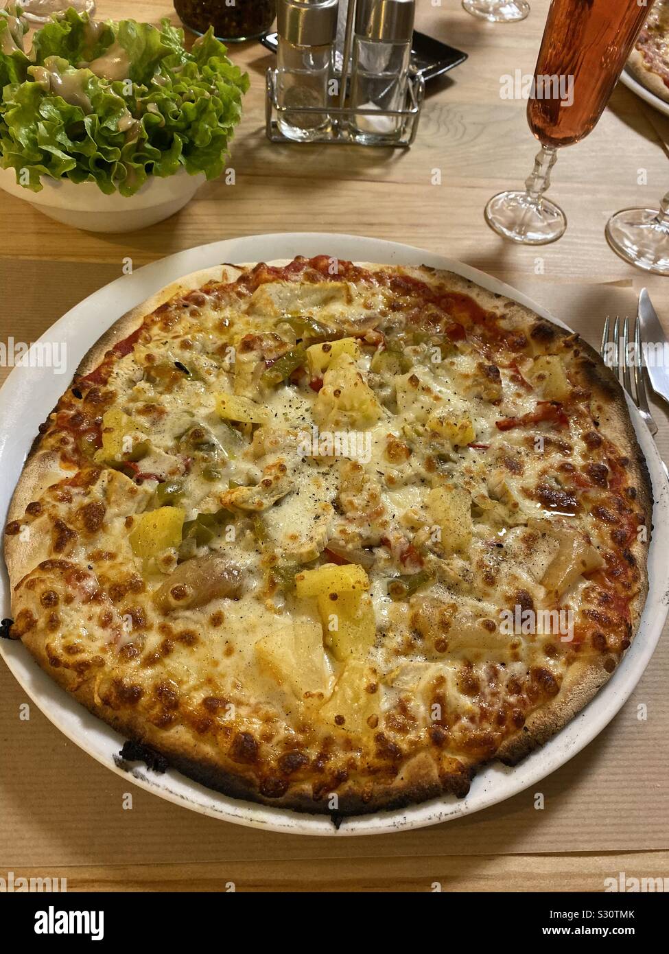 Hühnchen und Ananas Pizza in einem Restaurant mit Beilagen Salat und Wein Stockfoto