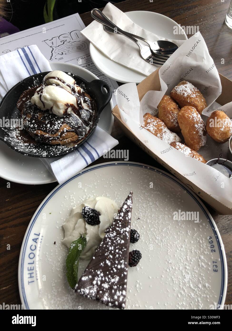 Eine Auswahl an Desserts im lokalen Restaurant in Wayland, Massachusetts: skillet Chocolate Chip Cookie Eisbecher mit Eis, flourless Schokolade Kuchen und eine Schachtel Donuts (BEIGNETS). Stockfoto