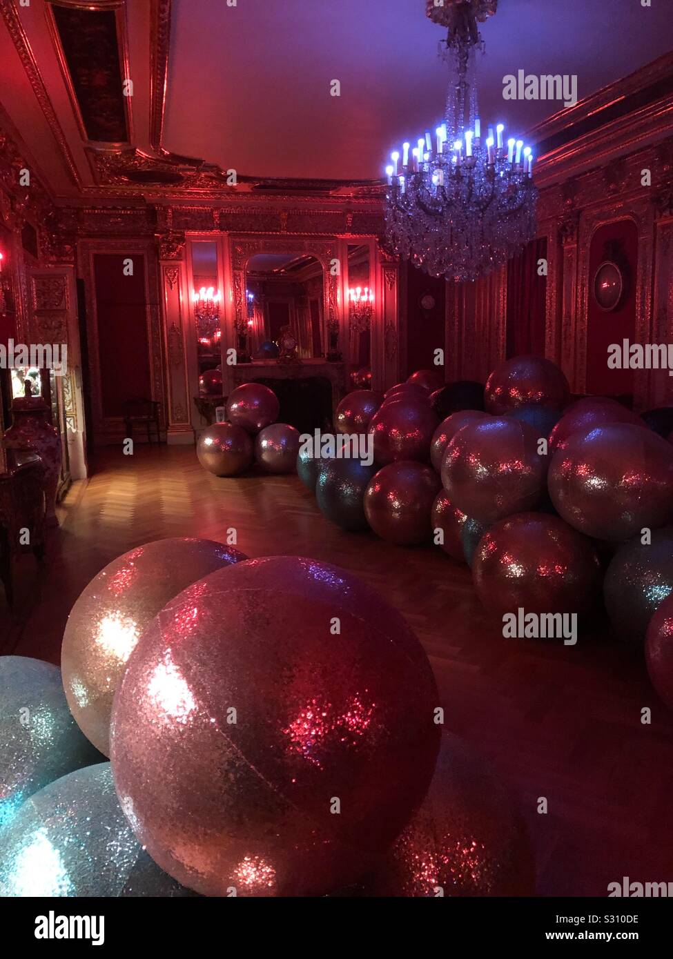 Riesige glitzernde Dekorative Christbaumkugeln angeordnet, die über den Fußboden eines Salons in einem englischen Herrenhaus im französischen Stil in der Nacht mit Kronleuchtern. Stockfoto