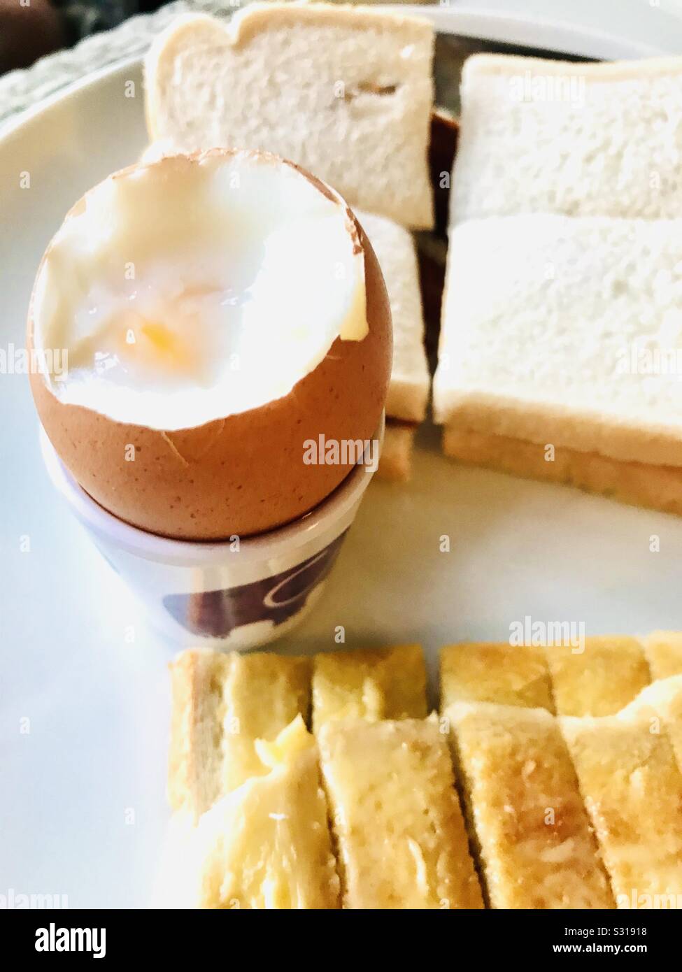 Gekochtes Ei mit gerösteten Soldaten und ein Schinken Sandwich im Hintergrund Stockfoto