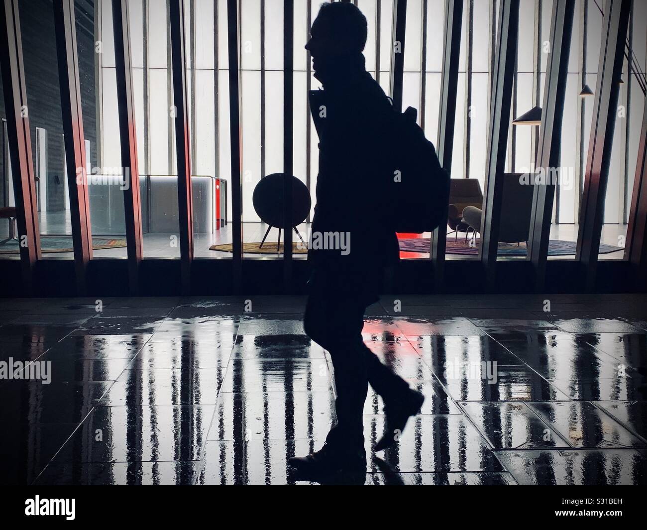 Silhouette der Mann vor einem Gebäude mit vertikalen Streifen in der Nacht an einem regnerischen Pflaster Stockfoto