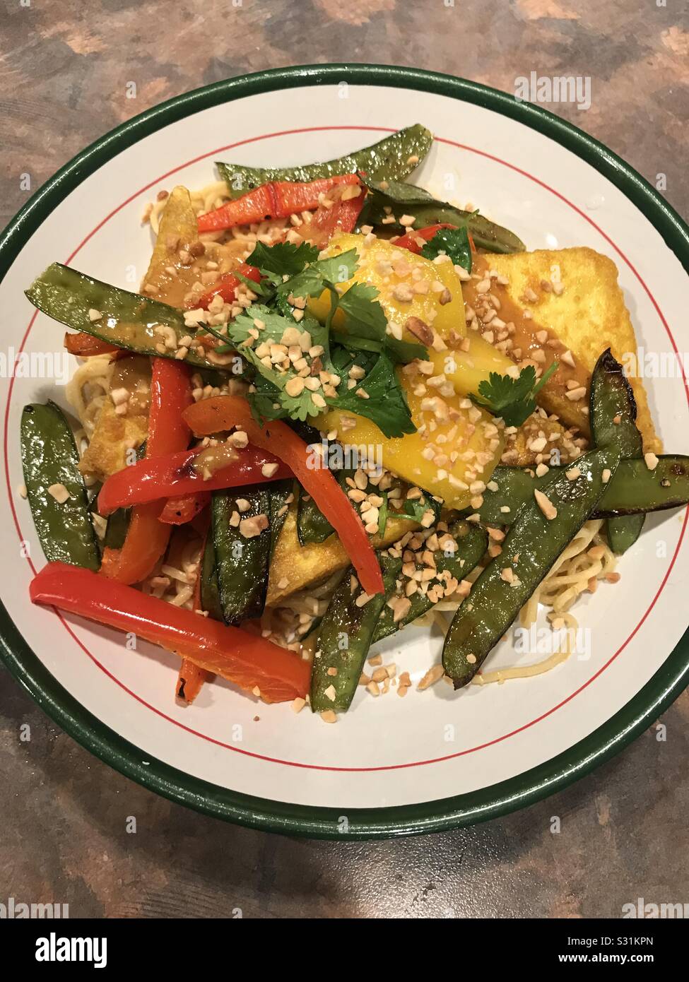 Veganer Hauptgericht-knuspriger Tofu mit roten Paprika für Schneepäen und Mangosalsa mit gehackten Erdnüssen über Nudeln. Stockfoto