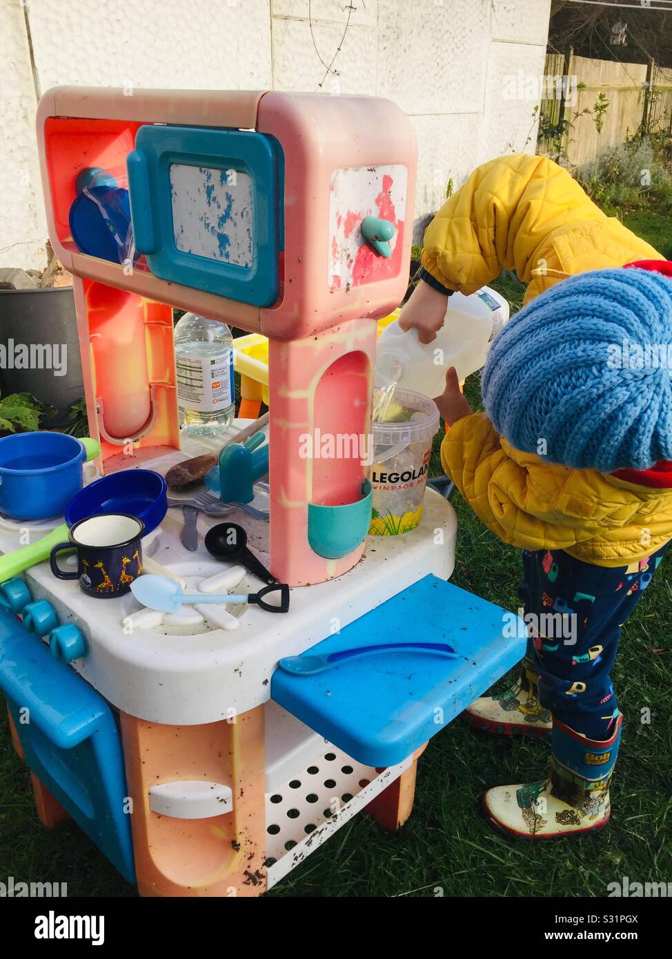 Kleinkind spielen messen Wasser spielen unordentlich Schlamm wasser Küche Garten im Freien junge WELLIES Stockfoto