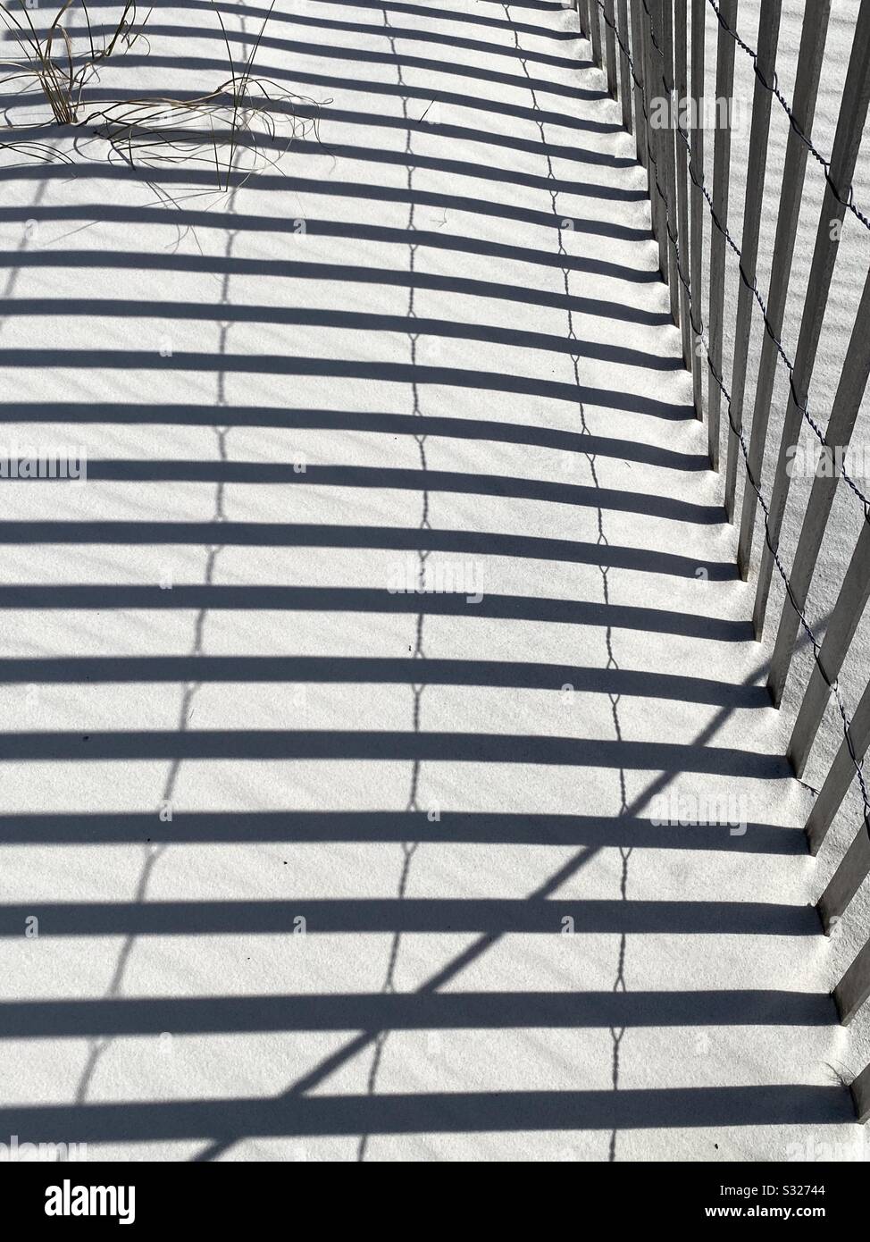 Von einem Holzzaun auf weißen Sandstrand gegossene Schattenlinien Stockfoto