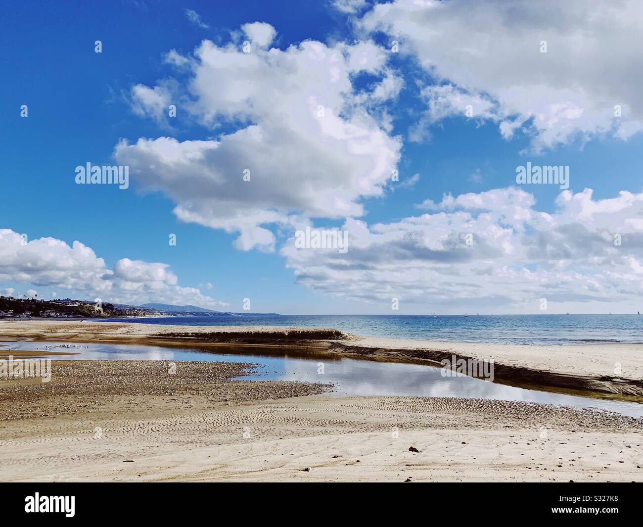 Sandstrand an einem sonnigen Tag mit weißen Wolken, die sich im Wasser spiegeln. - Smartphone-aufgenommenes Stockfoto