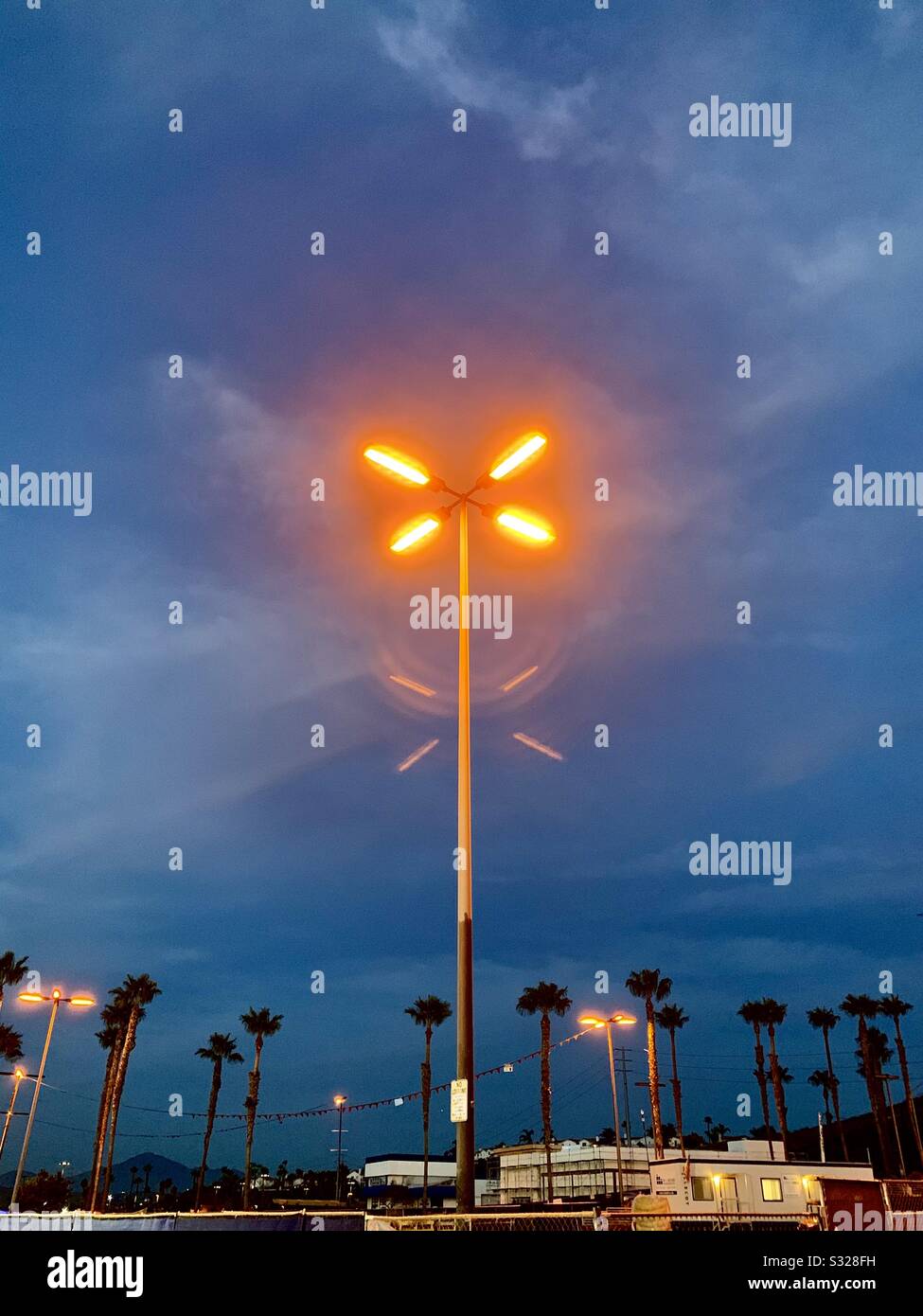 Auf einem Parkplatz scheint ein Leuchtstofflicht gegen einen bunten Abendhimmel. - Smartphone-aufgenommenes Stockfoto