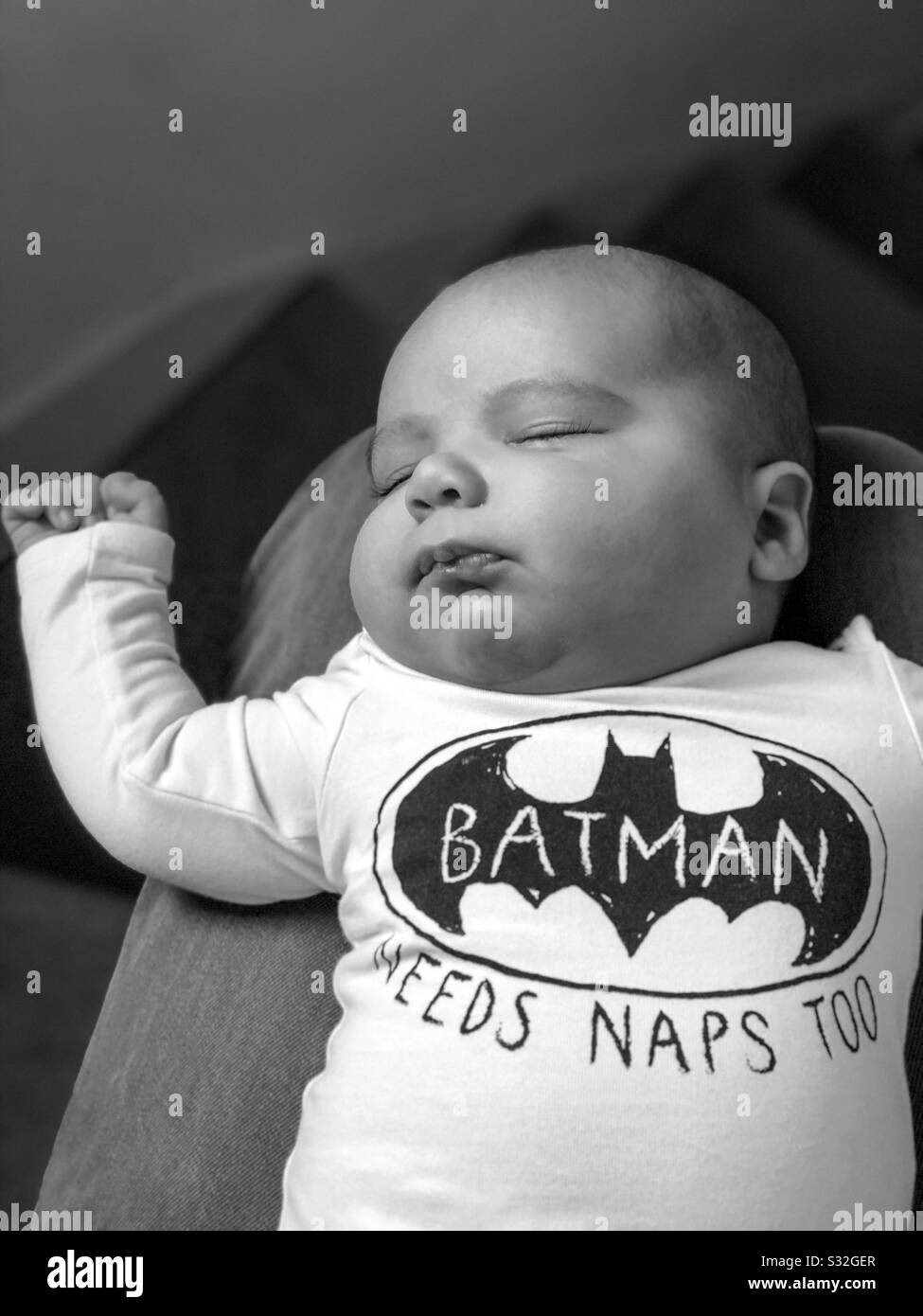 Ein 8-wöchiger alter Babyjunge, der auf dem Schoß seiner Väter nappt, während er als Batman verkleidet ist. Stockfoto