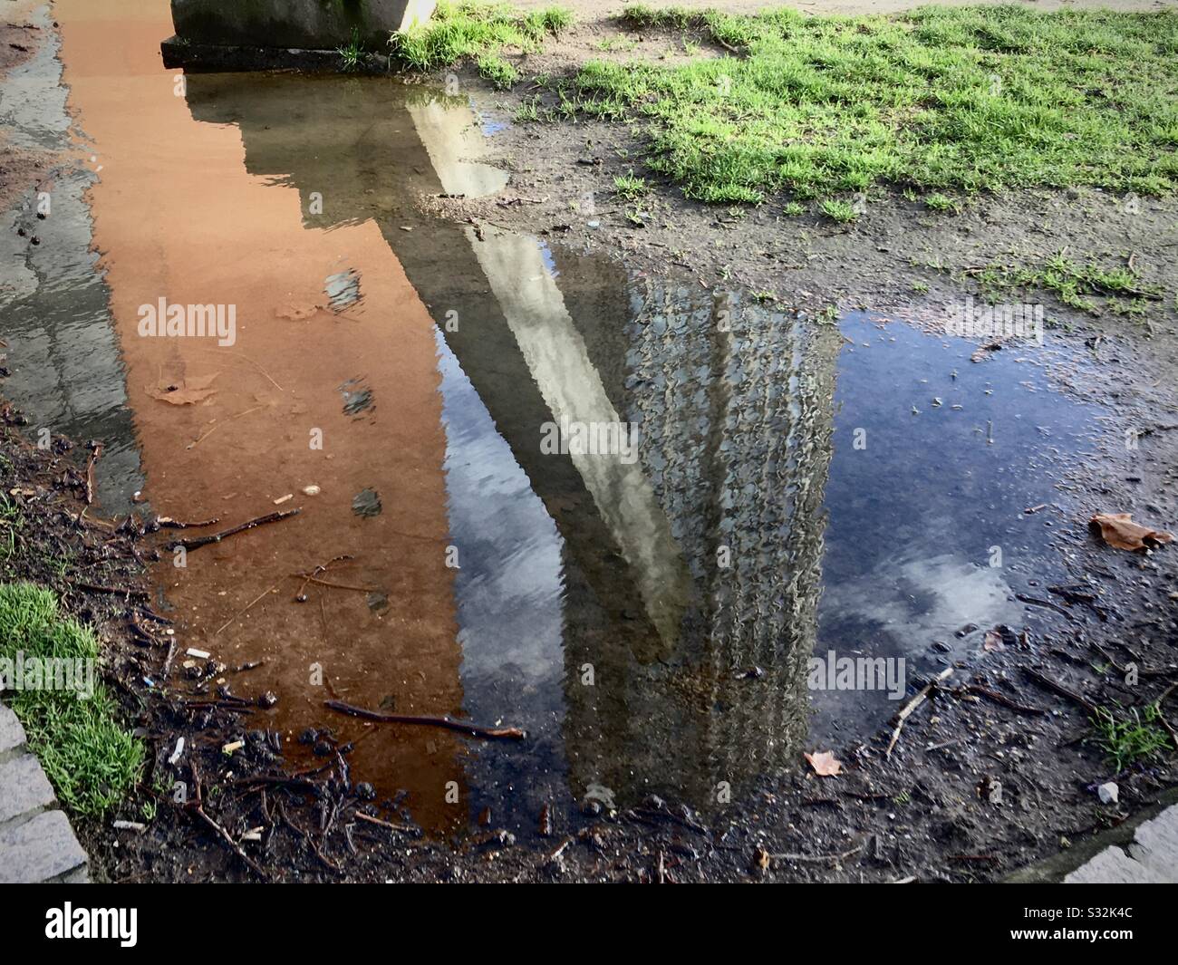 Reflexion von Stadtgebäuden und einem Bauwerk in einer Pfütze Stockfoto