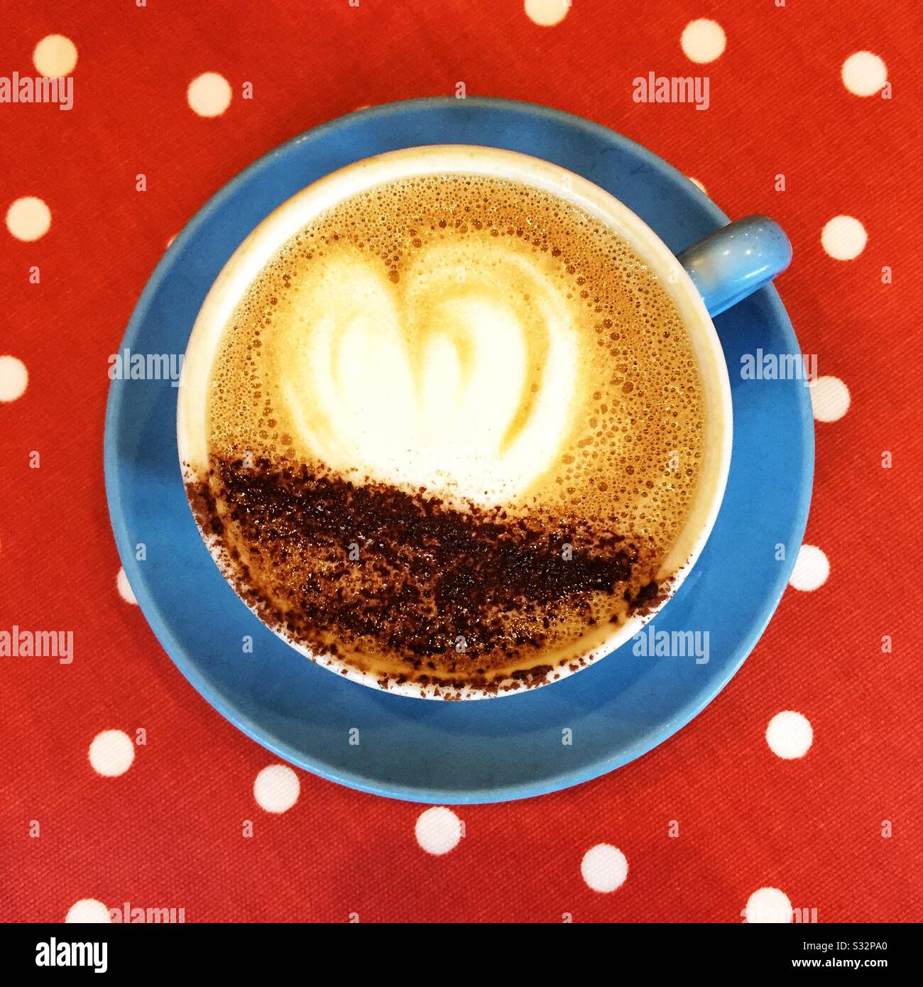Blick von oben auf einen matten Cappuccino-Kaffee mit Herzform auf der Oberfläche in einer farbenfrohen Tasse und Untertasse mit heißem Getränk und Kopierraum Stockfoto