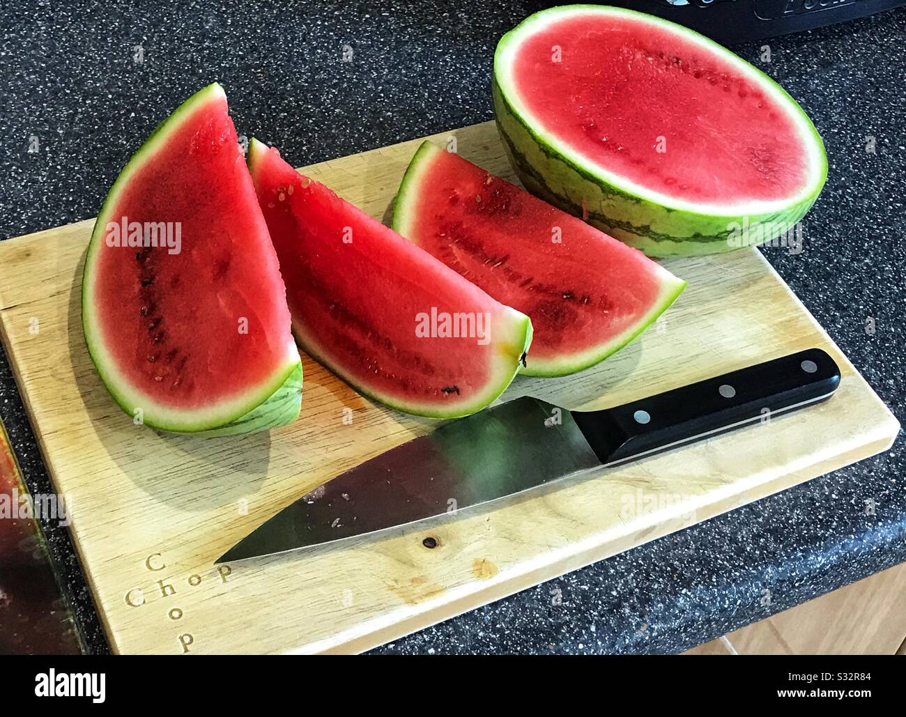 Wassermelonteil gehackt auf einem Holzhackbrett mit einem Messer sitzend - Smartphone-aufgenommenes Stockfoto