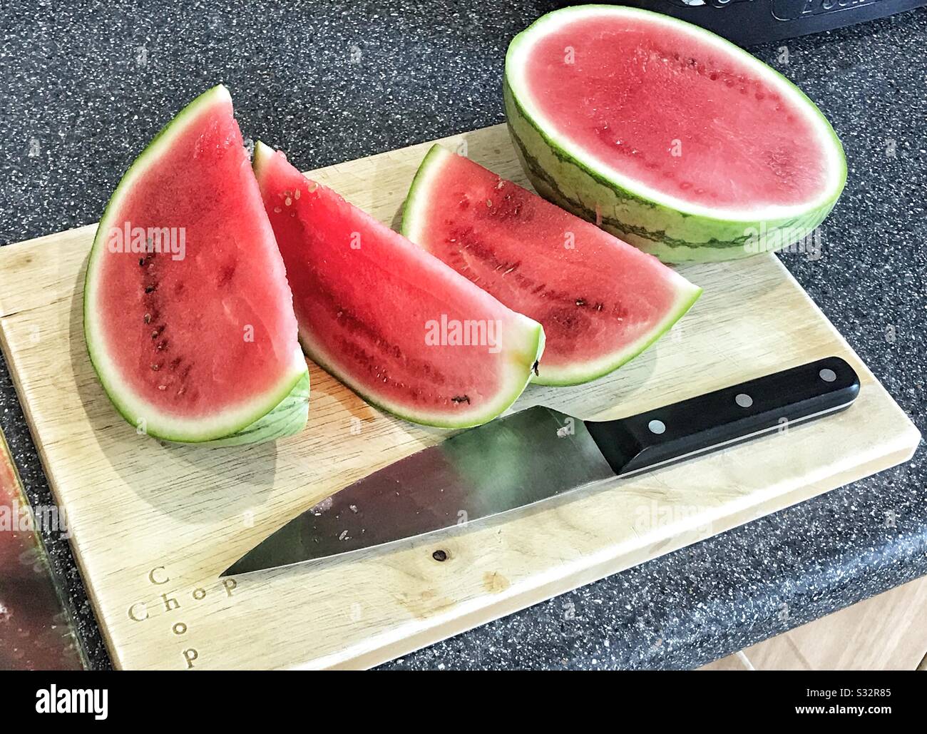 Wassermelonteil gehackt auf einem Holzhackbrett mit einem Messer sitzend - Smartphone-aufgenommenes Stockfoto