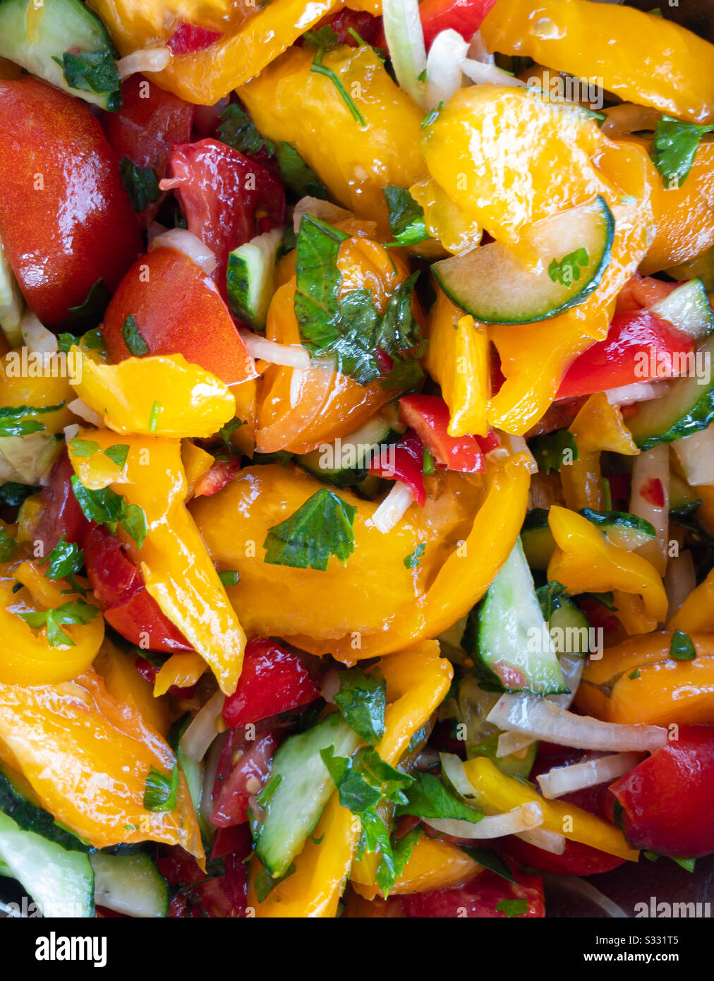 Draufsicht auf bunten veganen Salat mit roten und gelben Tomaten, Gurken, Zwiebeln und Grüns. Stockfoto