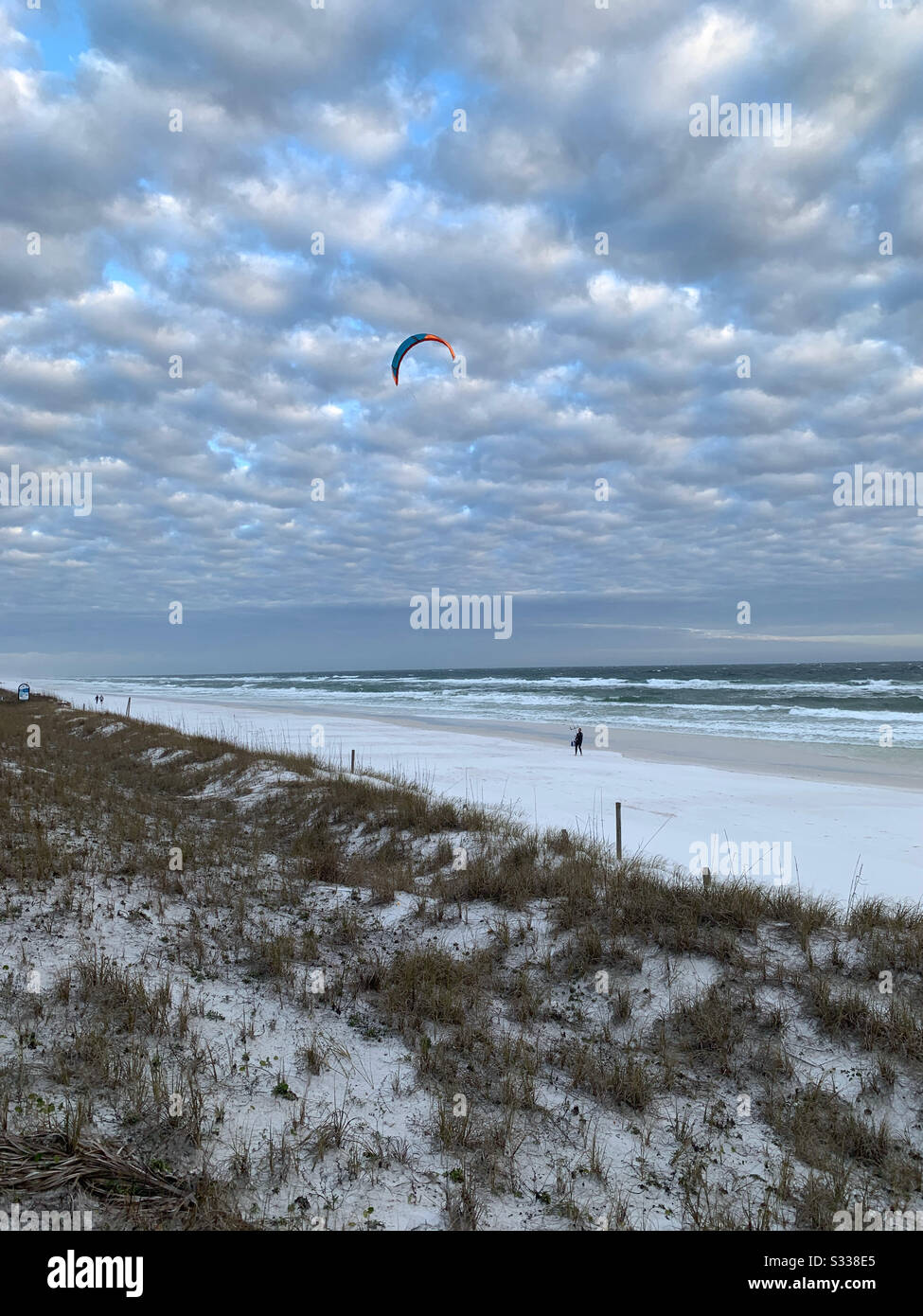 Weißer Sandstrand mit Blick auf Wasser, puffig weißer bewölkter Himmel und Kitesurfer - Smartphone-aufgenommenes Stockfoto