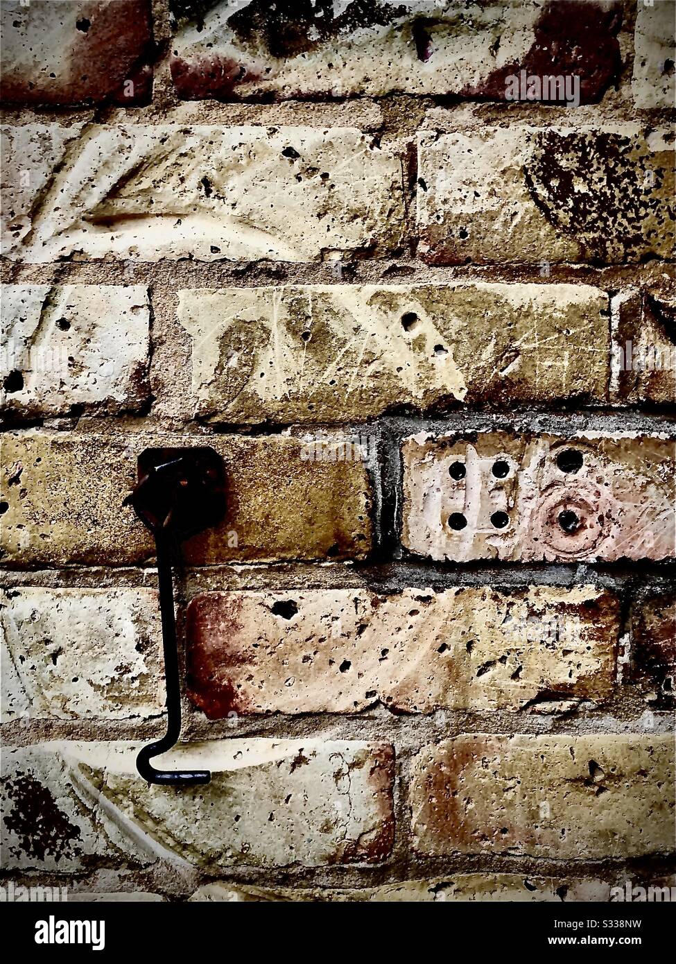 Die Mauer aus Backstein ist von der Metalltürverriegelung abgenutzt, die nach unten hängt. Andere Markierungen und Löcher erodierten und warnten in h Textur. Stockfoto